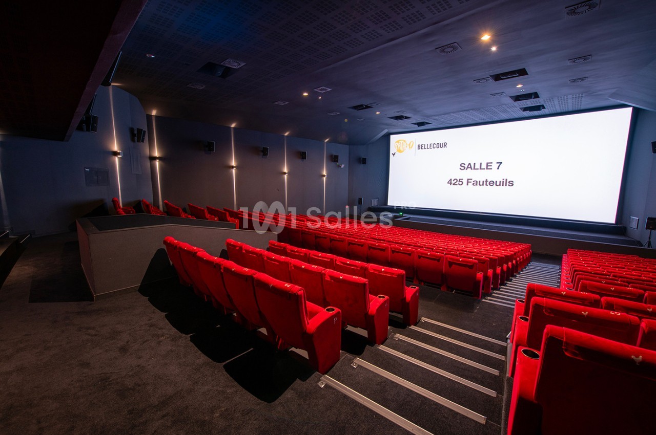 Salle de cinéma moderne avec des rangées de fauteuils rouges et un grand écran affichant ’Salle 7, 425 fauteuils’.