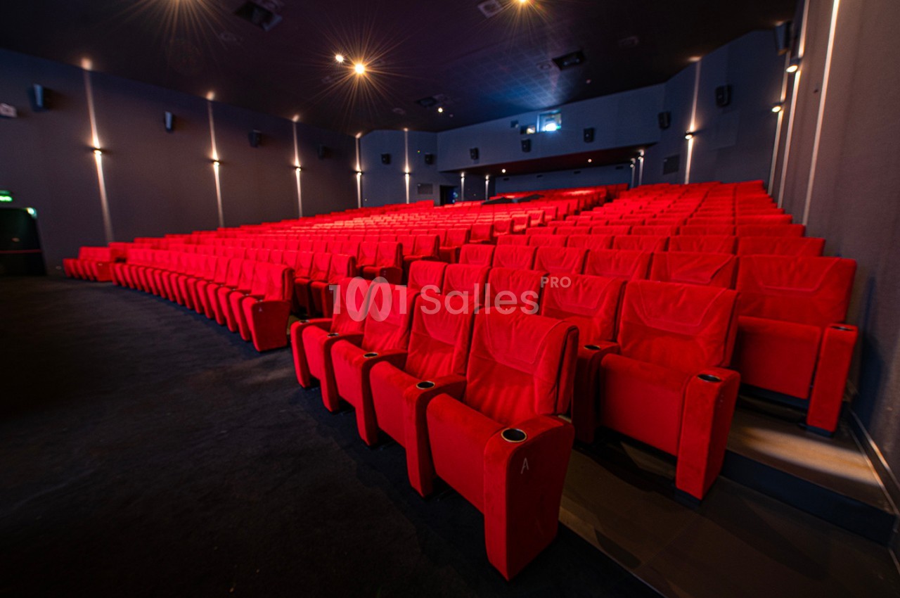Salle de cinéma vide avec des rangées de fauteuils rouges et un éclairage tamisé.