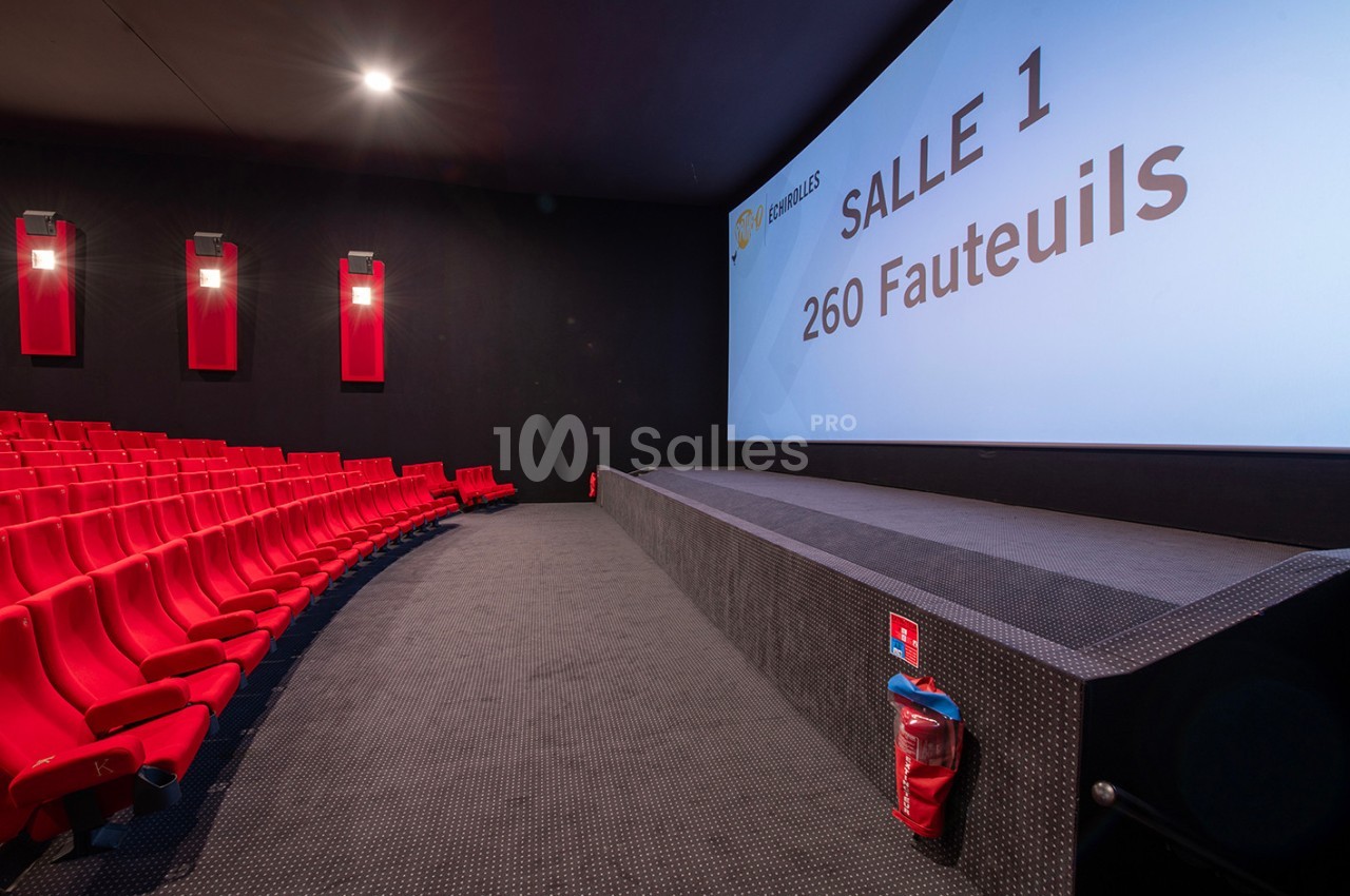 Salle de cinéma moderne avec sièges rouges, écran affichant ’Salle 1 - 260 fauteuils’ et extincteur au premier plan.