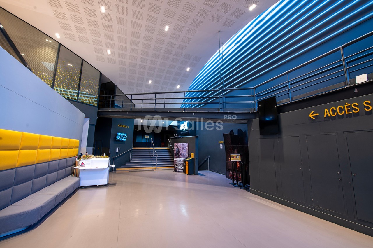 Hall moderne avec un comptoir d'accueil, des sièges gris et jaunes, un escalier et une signalisation ’Accès salles’.