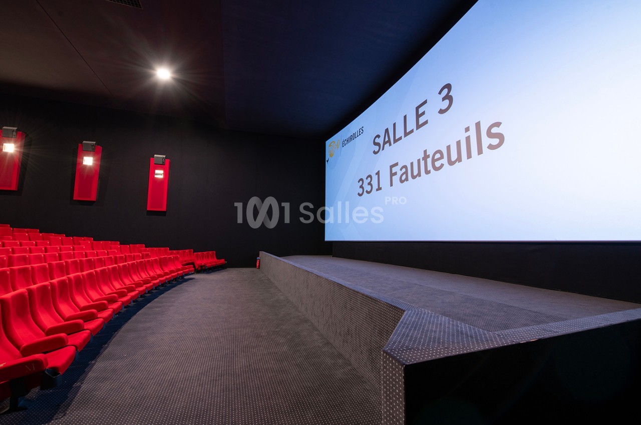 Salle de cinéma moderne avec sièges rouges, grand écran affichant ’Salle 3, 331 fauteuils’ et éclairage tamisé.