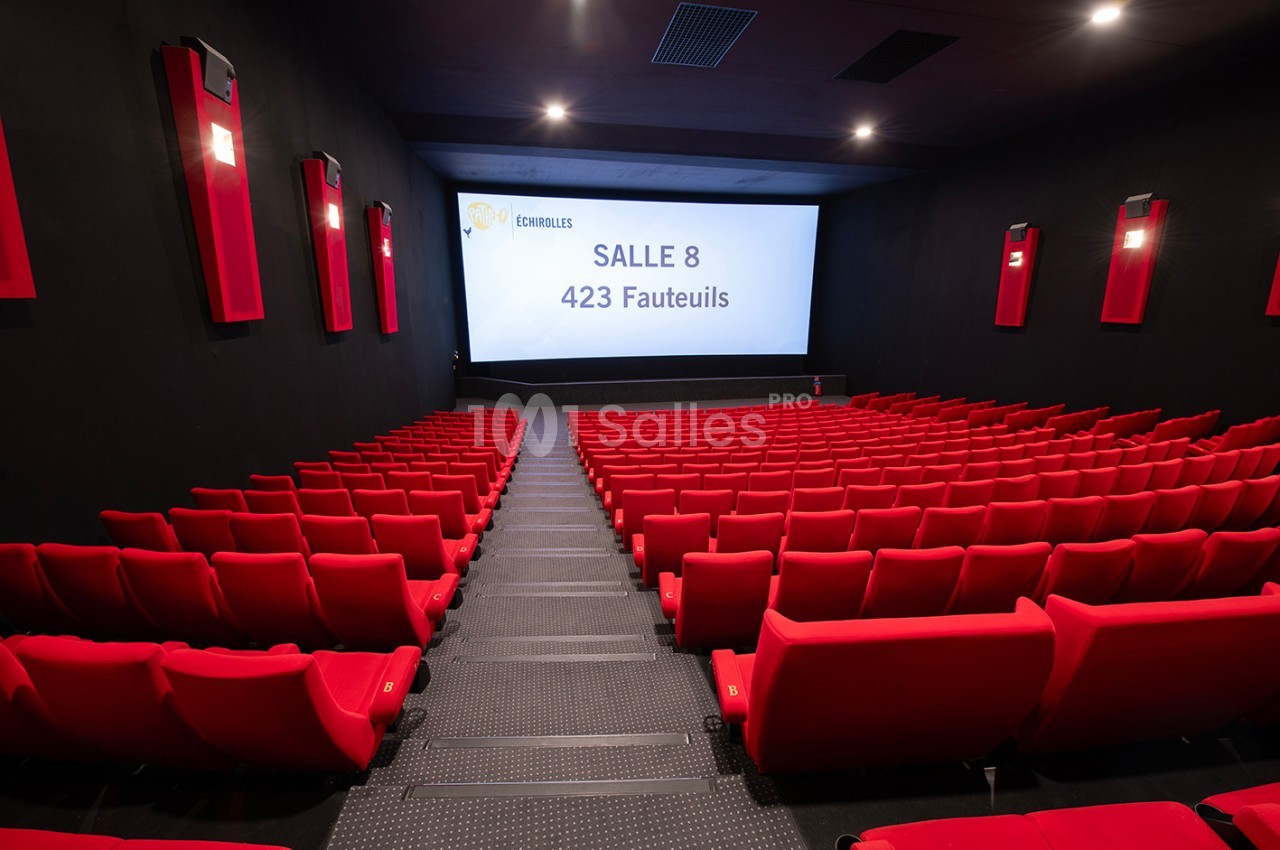 Salle de cinéma vide avec des rangées de fauteuils rouges et un écran affichant ’Salle 8, 423 fauteuils’.