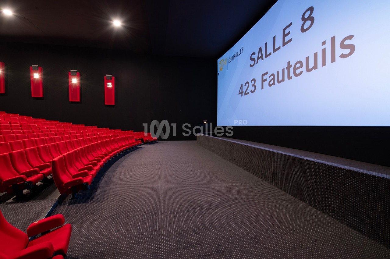 Salle de cinéma moderne avec des sièges rouges alignés et un écran affichant ’Salle 8, 423 fauteuils’.