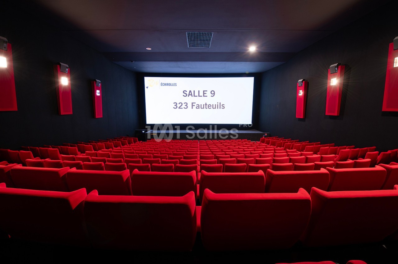 Salle de cinéma vide avec des rangées de fauteuils rouges et un écran affichant ’Salle 9, 323 fauteuils’.