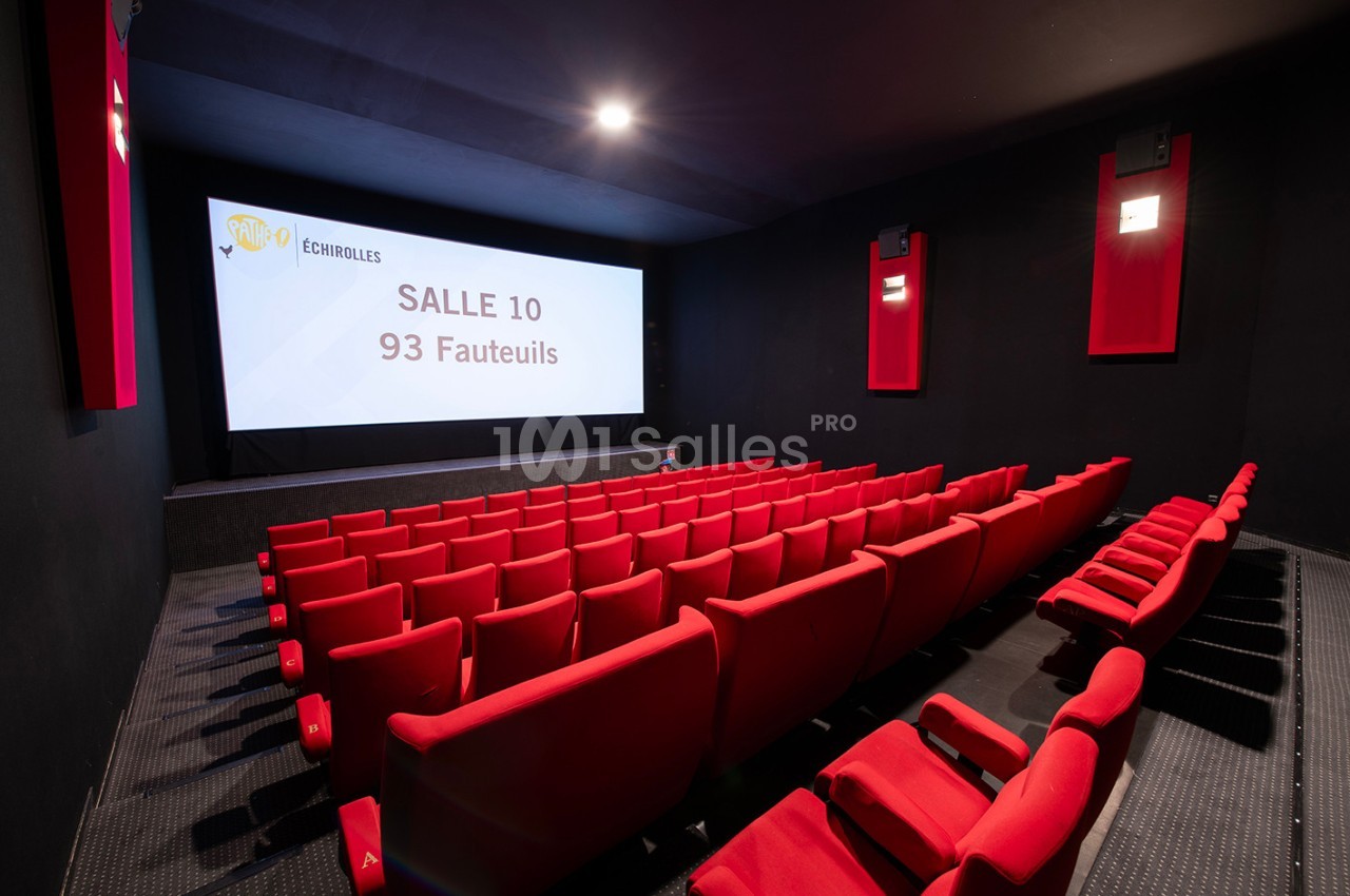 Salle de cinéma avec des rangées de fauteuils rouges, un écran affichant ’Salle 10, 93 fauteuils’ et un éclairage tamisé.