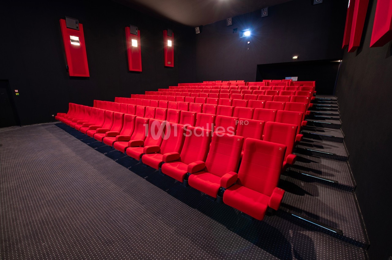 Salle de cinéma vide avec des rangées de sièges rouges et un éclairage tamisé.