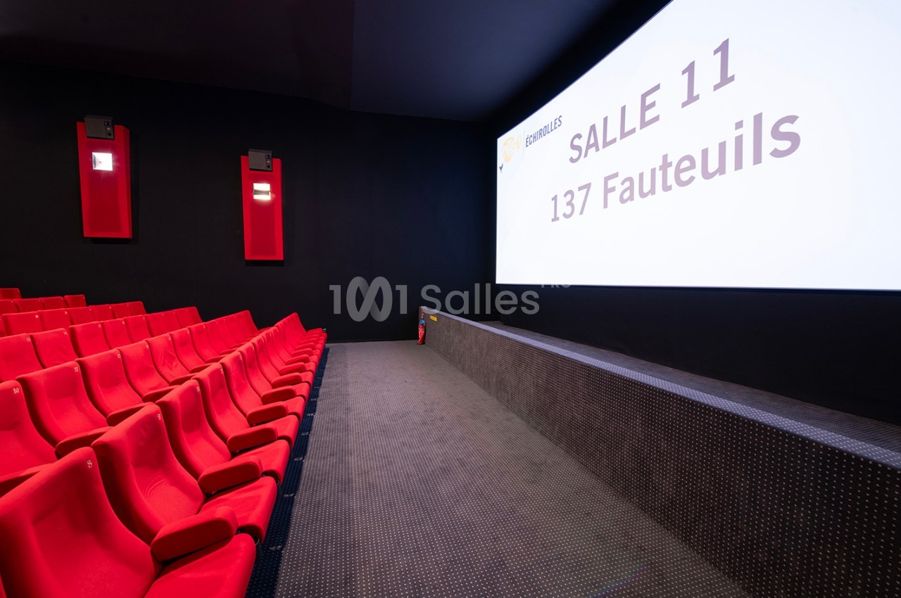 Salle de cinéma vide avec des sièges rouges, un écran affichant ’Salle 11, 137 fauteuils’ et un mur noir.