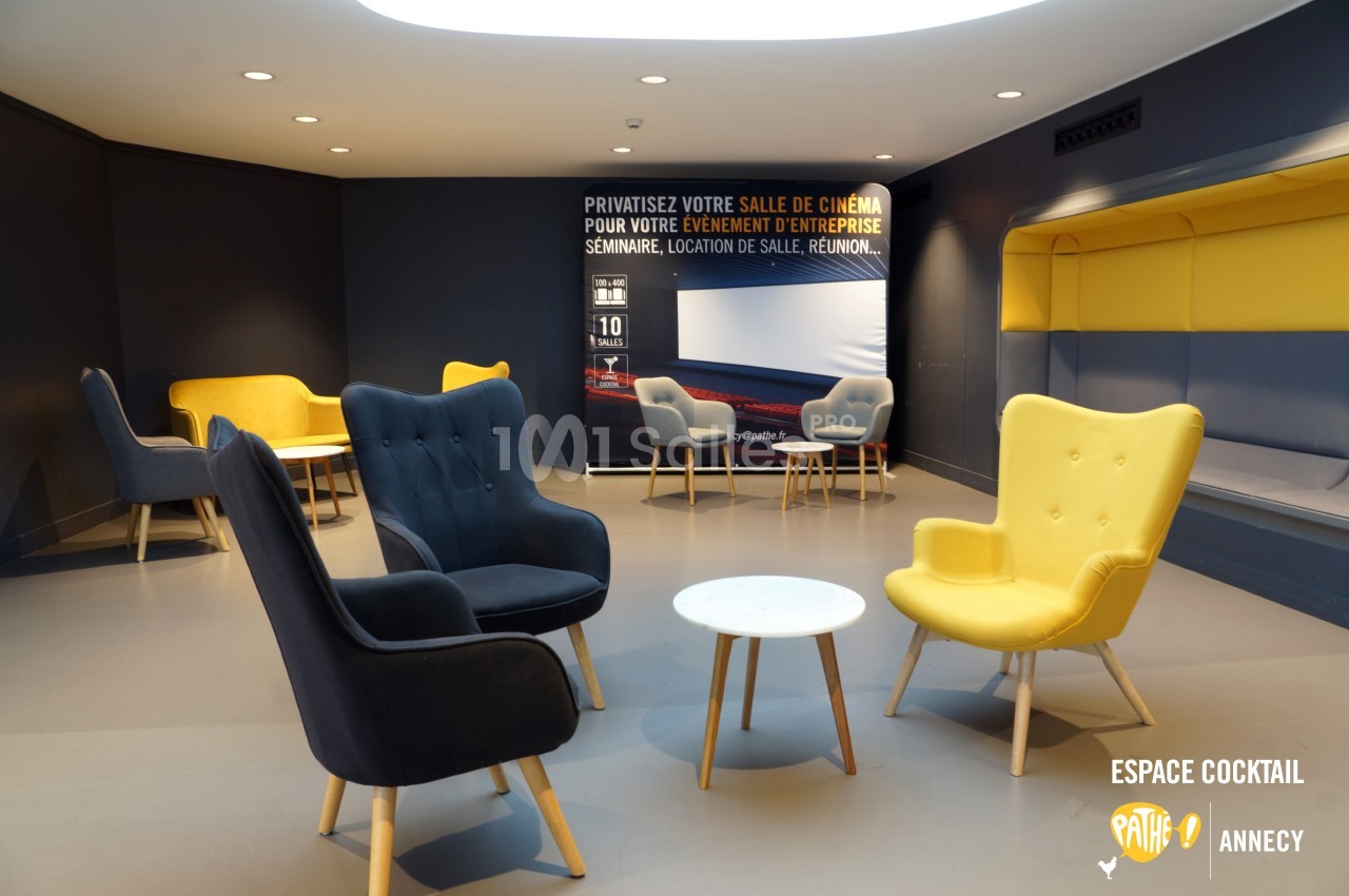 Espace lounge avec fauteuils colorés et table basse, devant un panneau promotionnel pour la privatisation d'une salle de…