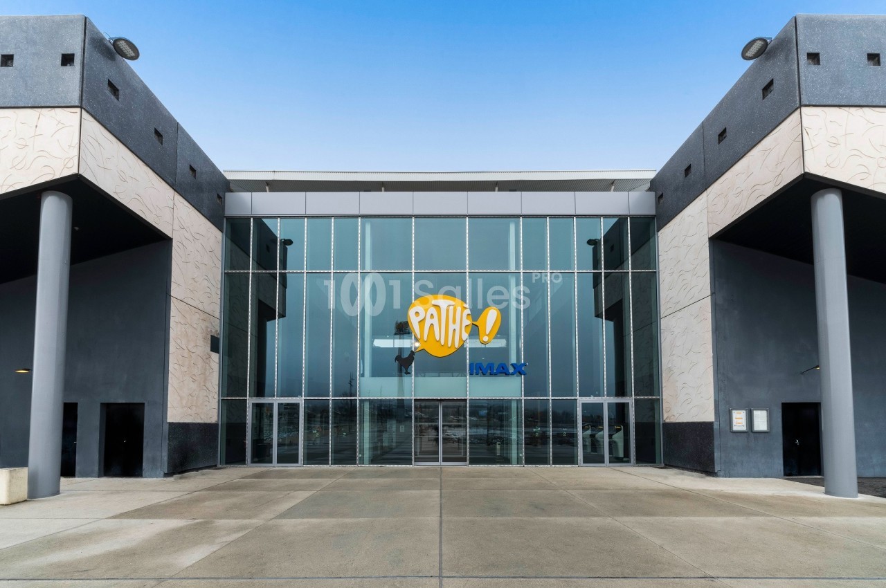 Façade vitrée d'un cinéma avec le logo Pathé et IMAX, entourée de murs gris et d'un sol en béton.