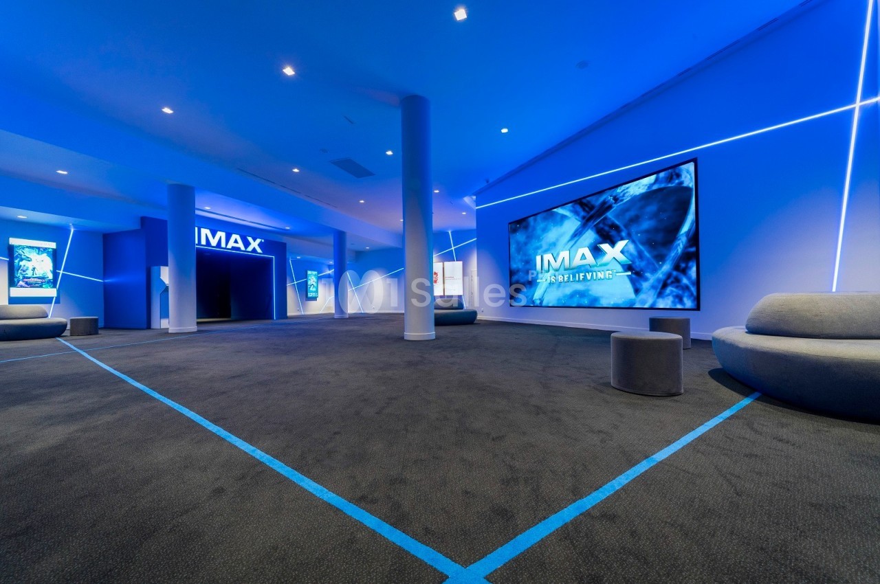 Salle de cinéma moderne avec éclairage bleu, écrans IMAX et sièges minimalistes.