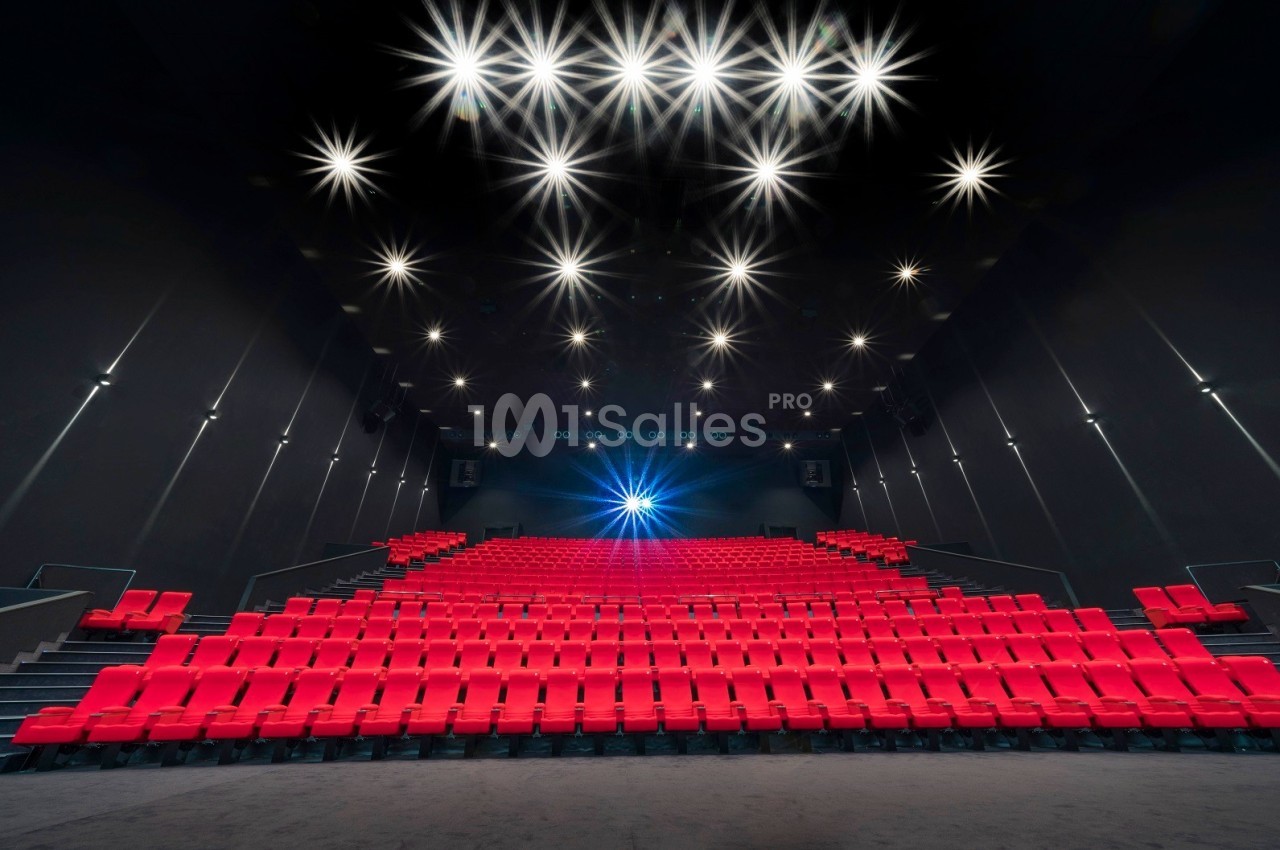 Salle de cinéma vide avec des rangées de sièges rouges et un éclairage lumineux au plafond.
