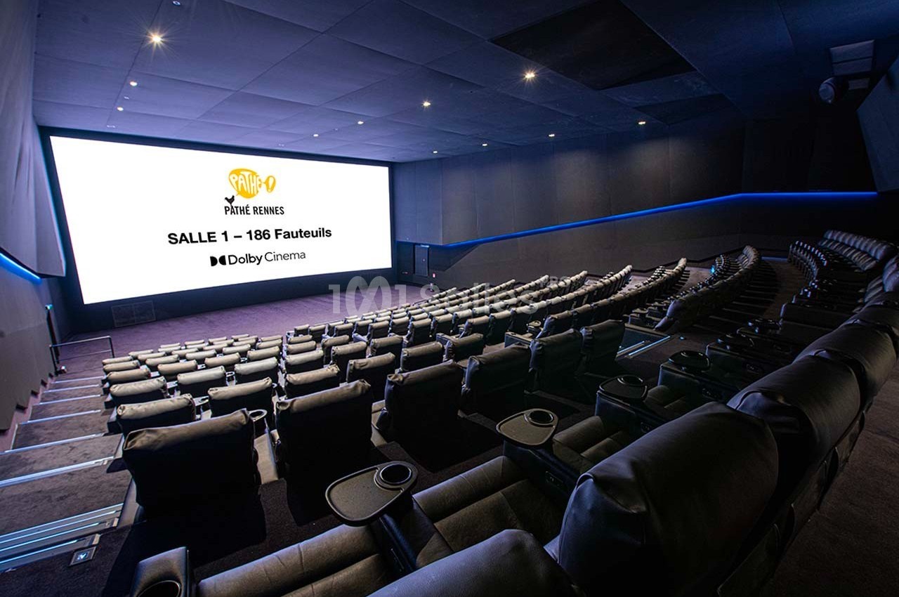 Salle de cinéma moderne avec fauteuils inclinables et grand écran affichant des informations sur la salle.