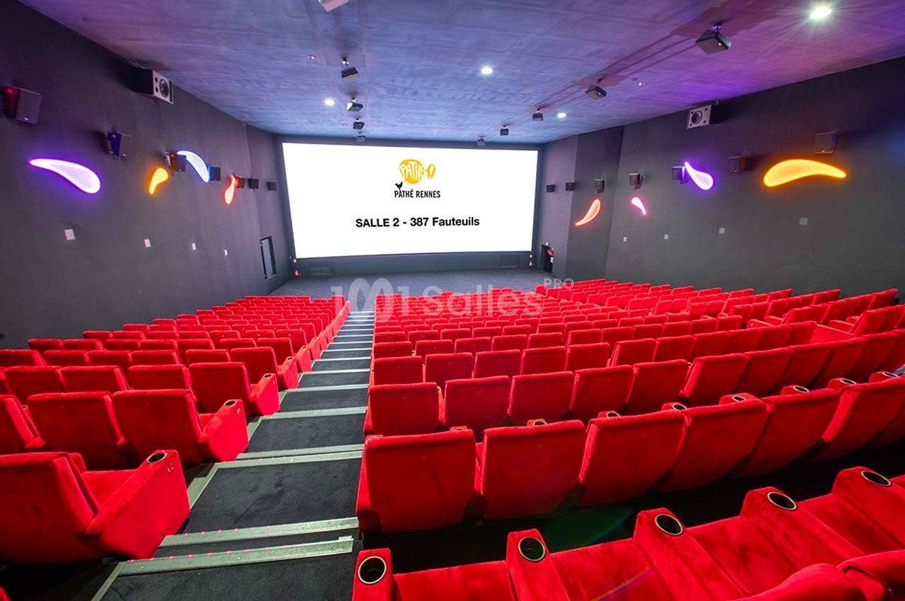 Salle de cinéma vide avec des rangées de fauteuils rouges et un écran affichant ’Salle 2 - 387 fauteuils’.