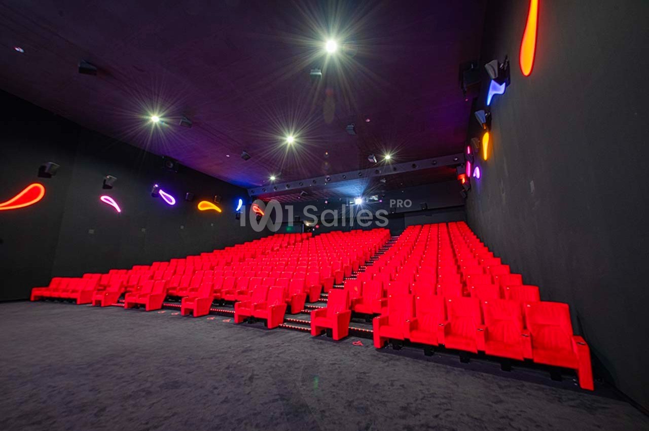 Salle de cinéma vide avec rangées de fauteuils rouges et éclairage néon coloré sur les murs sombres.