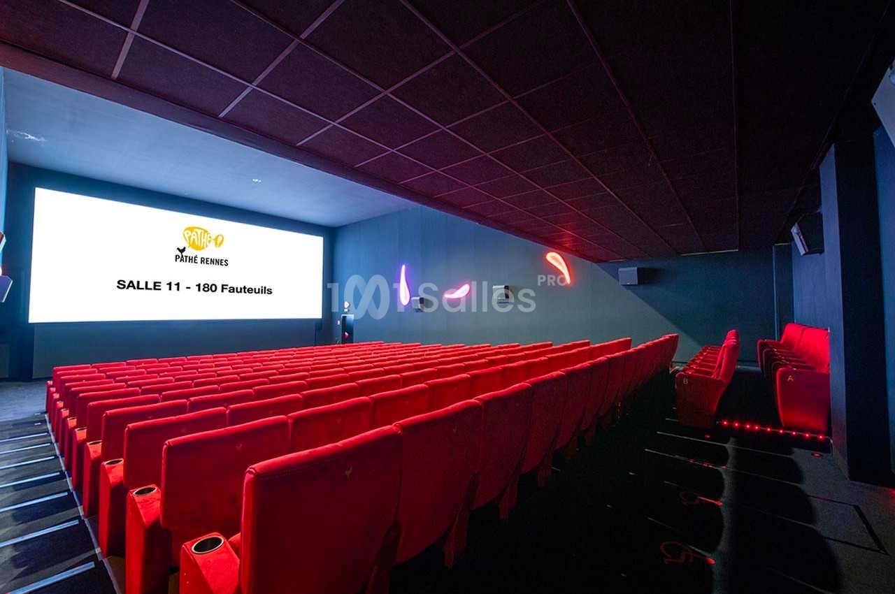 Salle de cinéma vide avec des rangées de fauteuils rouges et un écran blanc affichant des informations.
