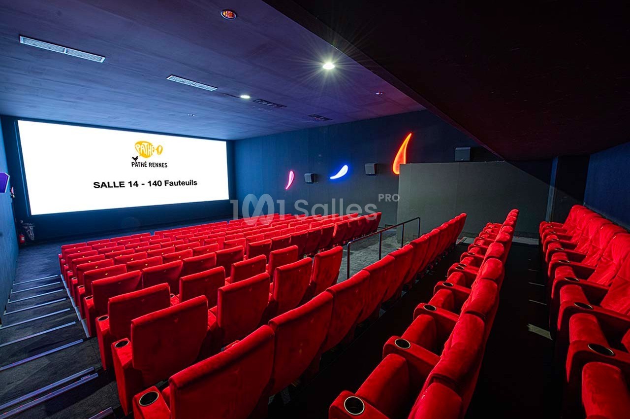 Salle de cinéma vide avec des sièges rouges alignés face à un grand écran affichant ’Salle 14 - 140 Fauteuils’.