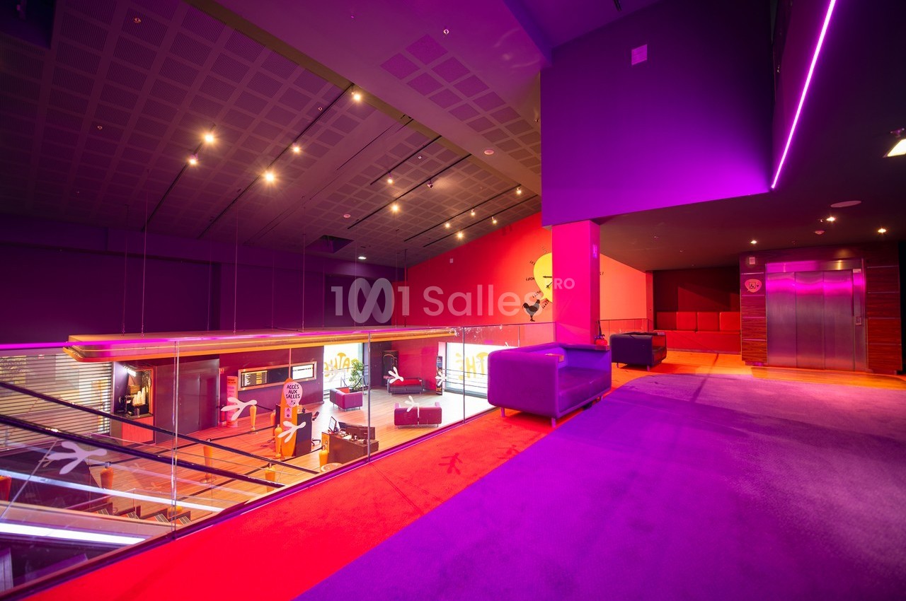 Intérieur moderne avec éclairage violet et rouge, canapé, ascenseur et vue sur un espace en mezzanine.