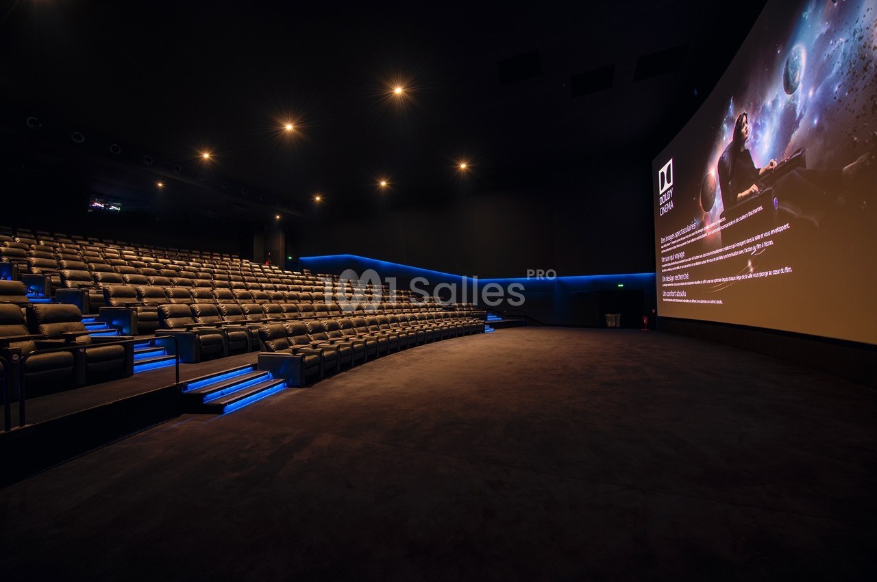 Salle de cinéma moderne avec sièges inclinés, éclairage tamisé et grand écran affichant une image spatiale.