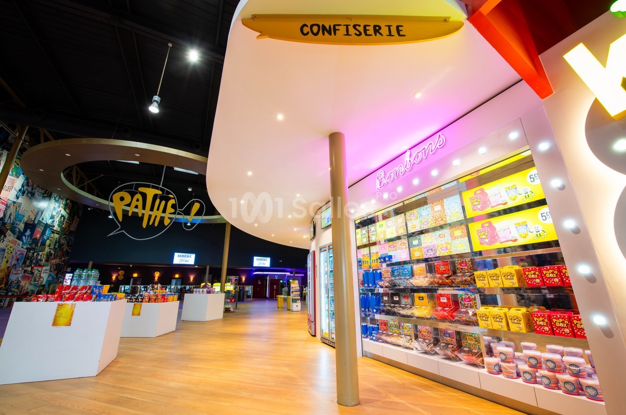 Rayon de confiseries colorées dans un hall lumineux avec signalétique et enseigne Pathé en arrière-plan.