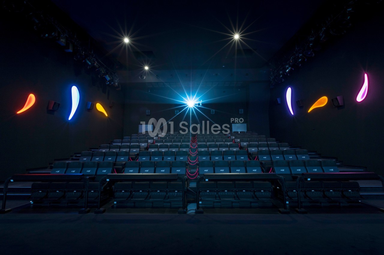 Salle de cinéma vide avec rangées de sièges alignés et éclairage coloré sur les murs sombres.