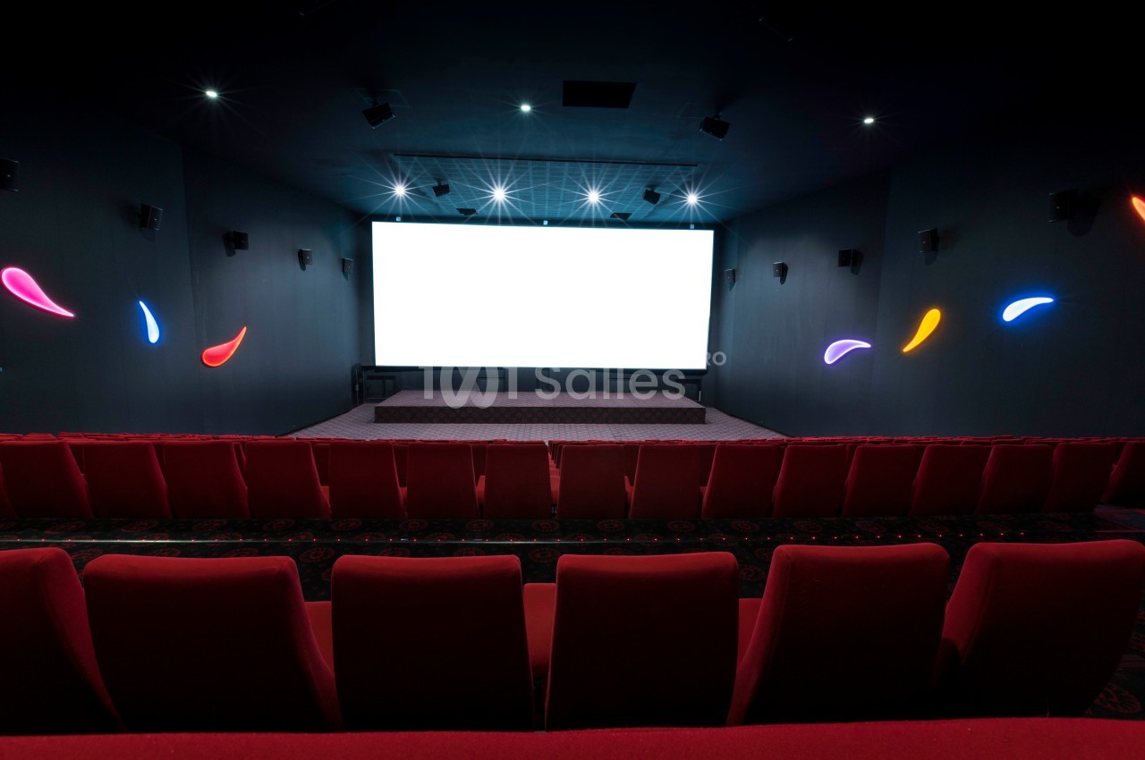 Salle de cinéma vide avec écran blanc allumé, sièges rouges et éclairages muraux colorés.