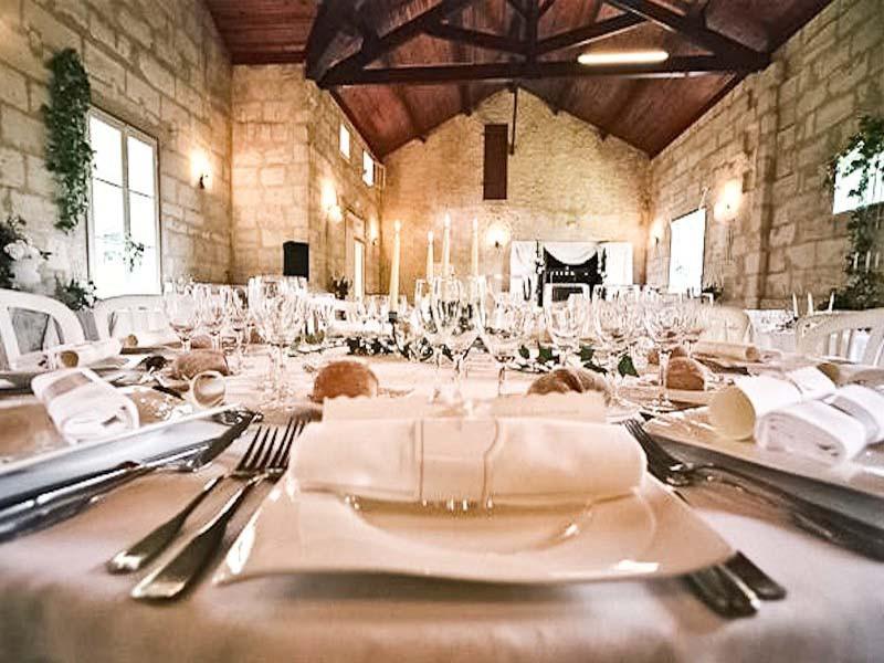 Salle de réception décorée avec des tables élégamment dressées, nappes blanches et chandeliers, ambiance chaleureuse.