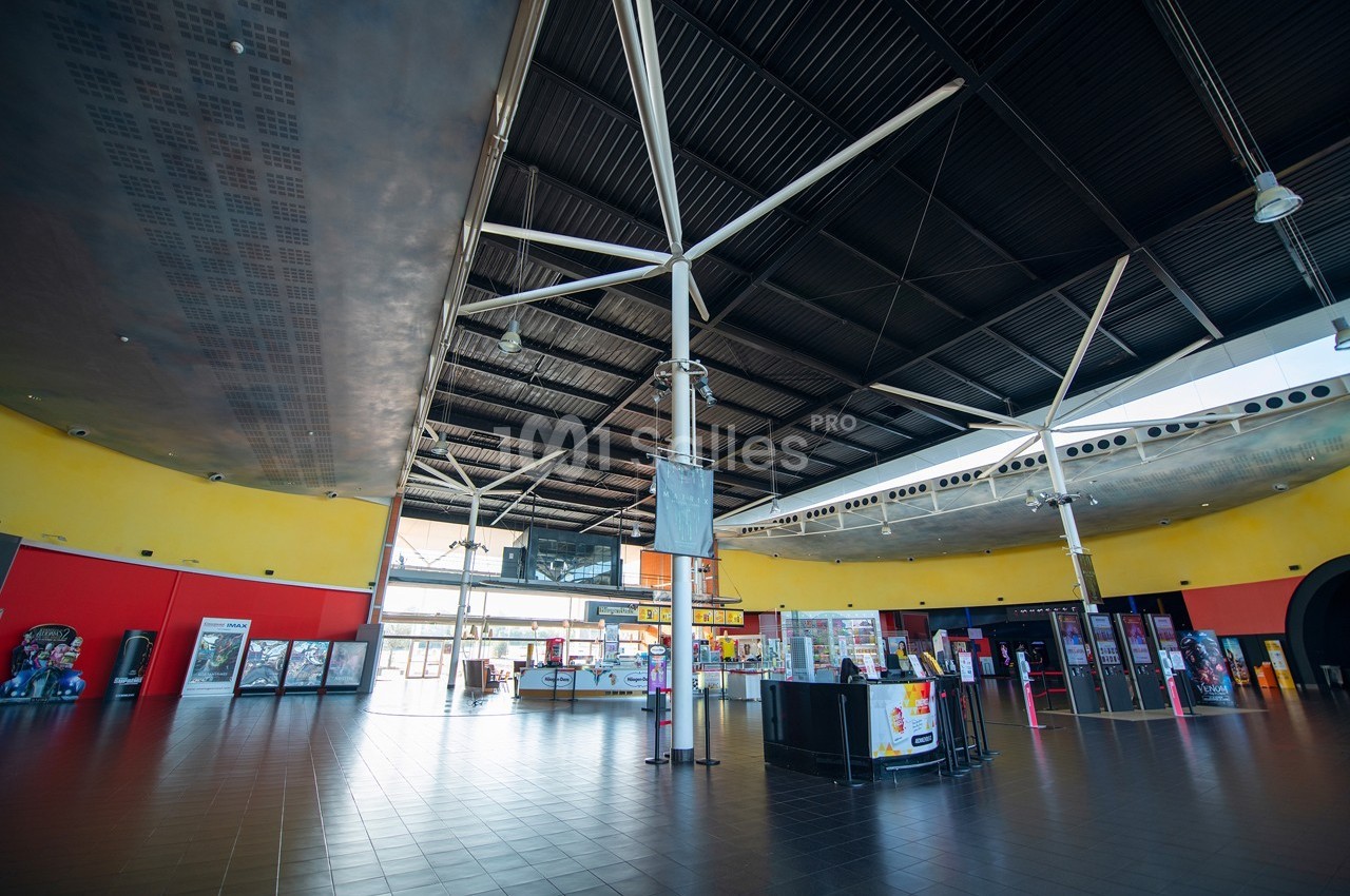 Intérieur spacieux d'un bâtiment avec plafond métallique, murs colorés et bornes de jeux alignées.