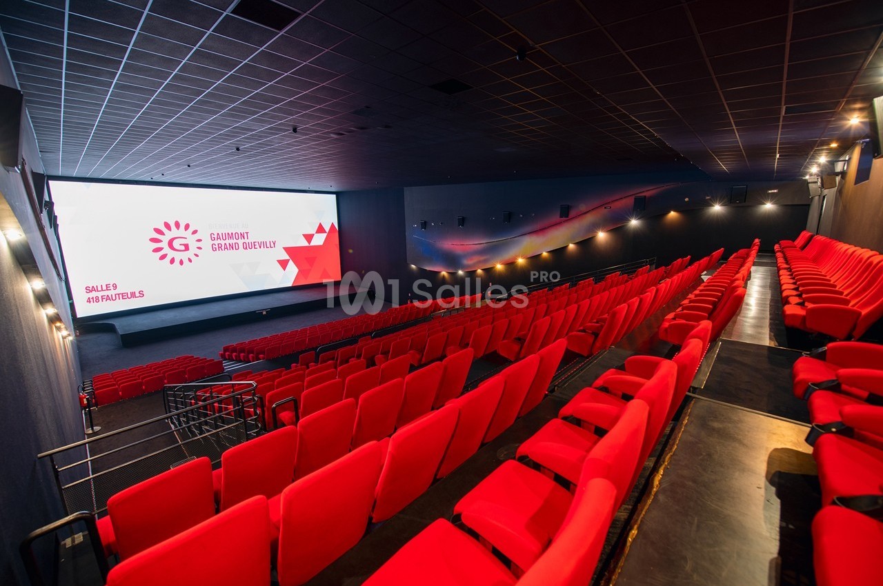 Salle de cinéma moderne avec rangées de sièges rouges et grand écran allumé affichant des informations.