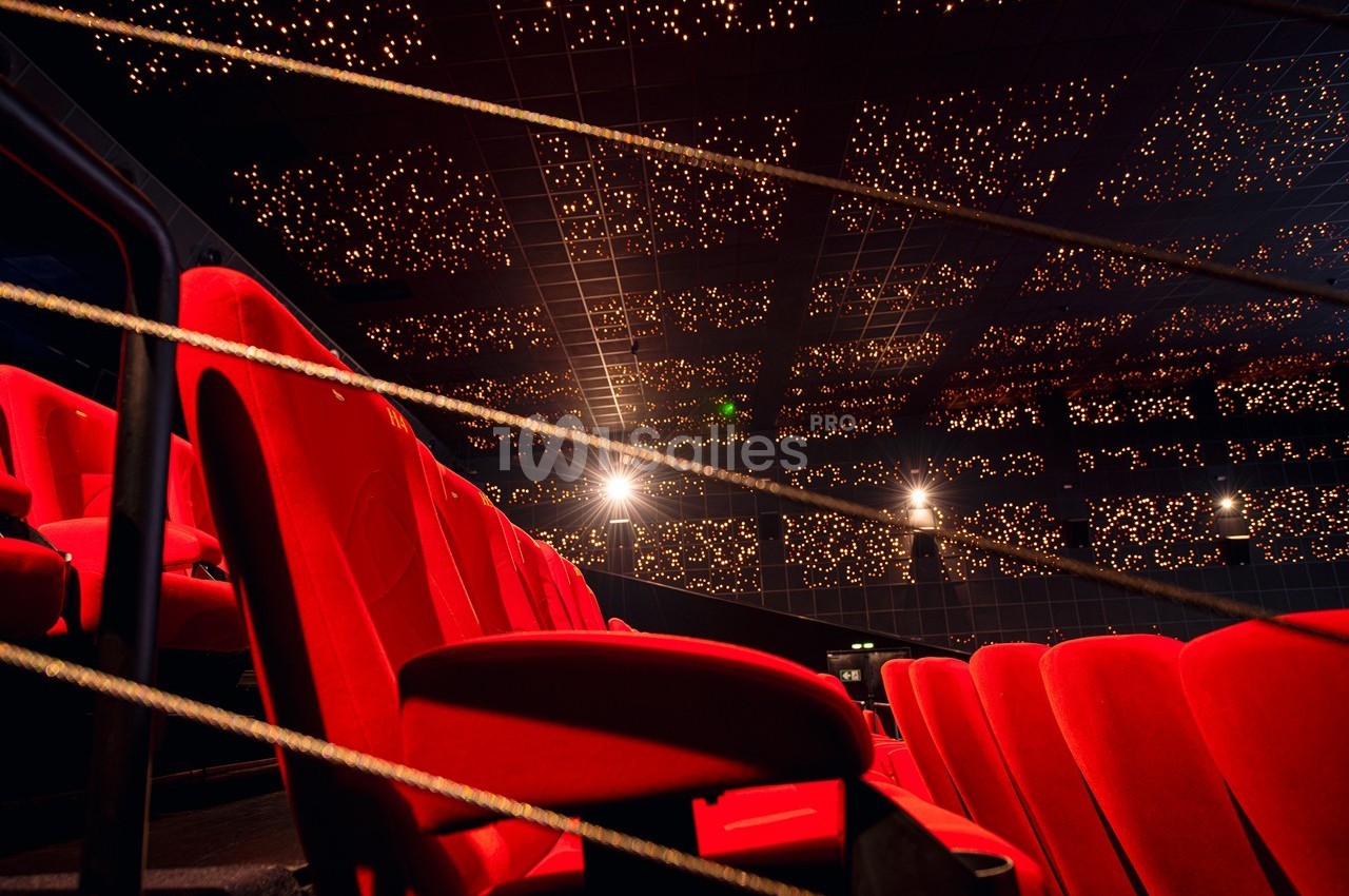 Rangées de fauteuils rouges dans une salle de cinéma avec un plafond illuminé de petites lumières.