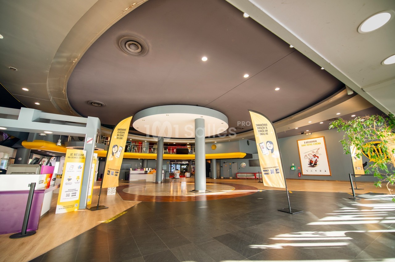 Hall spacieux d'un bâtiment moderne avec des colonnes, des affiches promotionnelles et un sol en bois et carrelage.