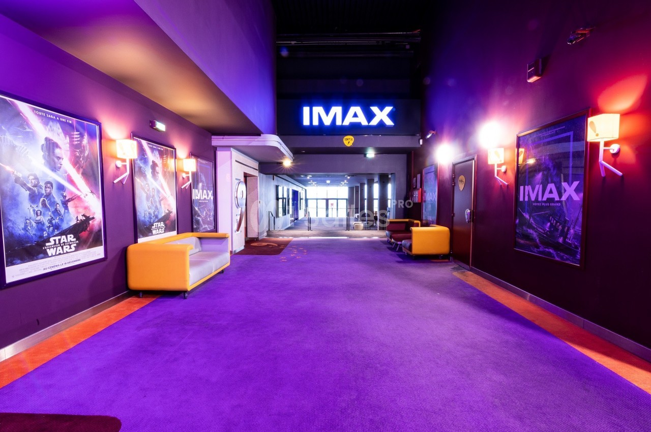 Couloir d'entrée d'un cinéma IMAX avec affiches de films sur les murs et fauteuils colorés.