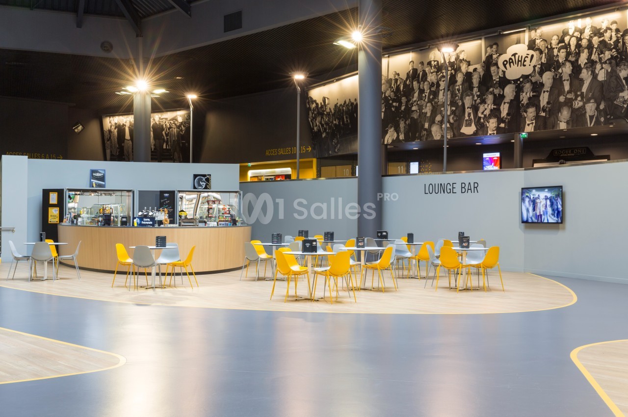 Espace lounge avec tables et chaises jaunes, comptoir de bar en arrière-plan et décoration murale en noir et blanc.