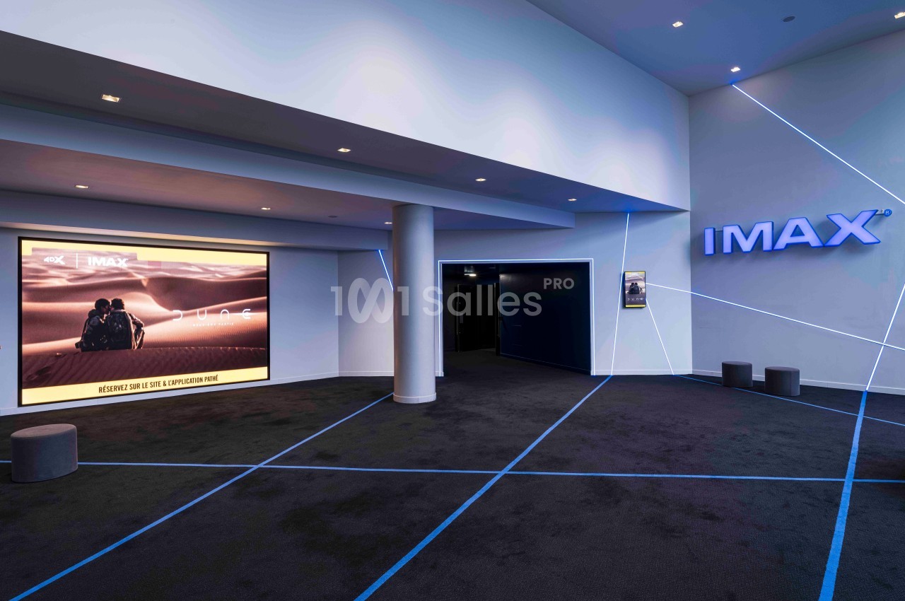 Entrée d'une salle IMAX avec un écran affichant une affiche de film et des lignes lumineuses au sol et sur les murs.