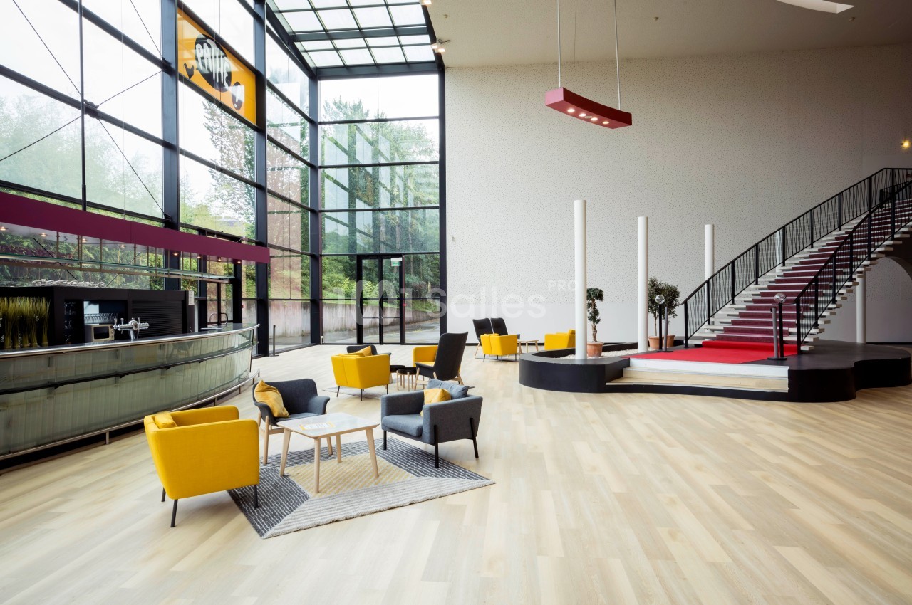 Intérieur lumineux avec escalier, mobilier moderne coloré et grandes baies vitrées donnant sur un espace arboré.