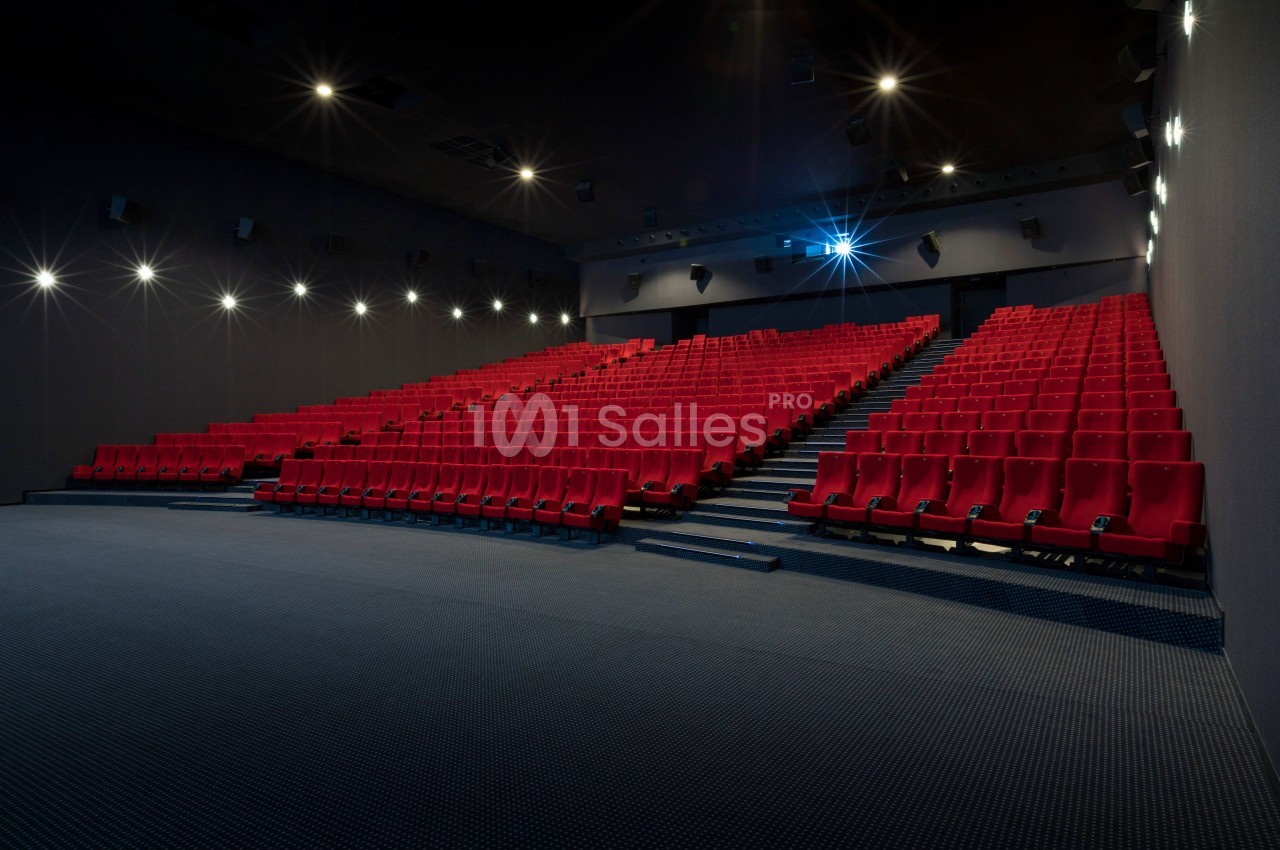 Salle de cinéma vide avec des rangées de sièges rouges et un projecteur allumé.