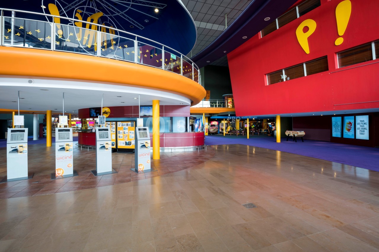 Hall spacieux d'un cinéma avec bornes automatiques, comptoirs de confiserie et décorations colorées.