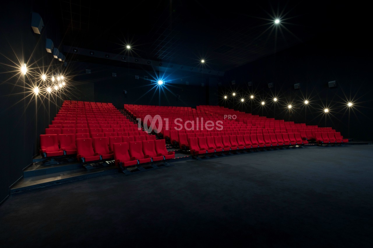 Salle de cinéma vide avec des rangées de sièges rouges et un éclairage tamisé.