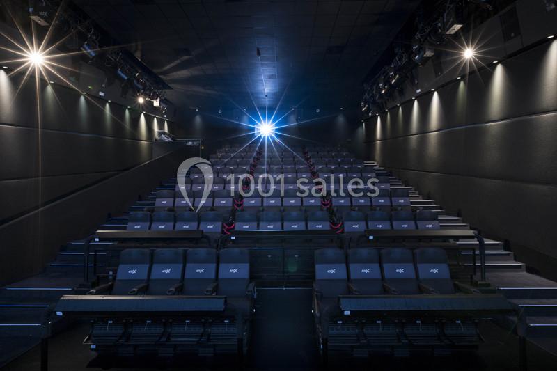 Salle de cinéma vide avec rangées de sièges alignés, éclairage tamisé et projecteur allumé au fond.