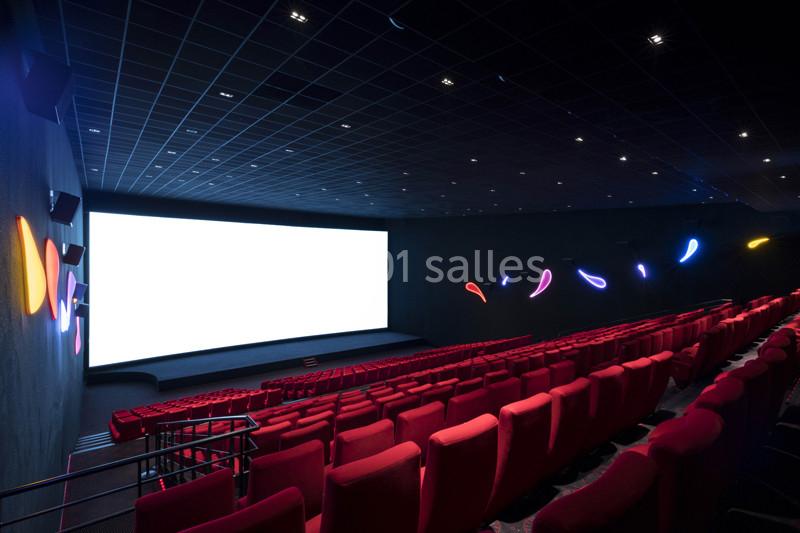 Salle de cinéma vide avec des rangées de sièges rouges, un grand écran blanc et des lumières décoratives colorées.