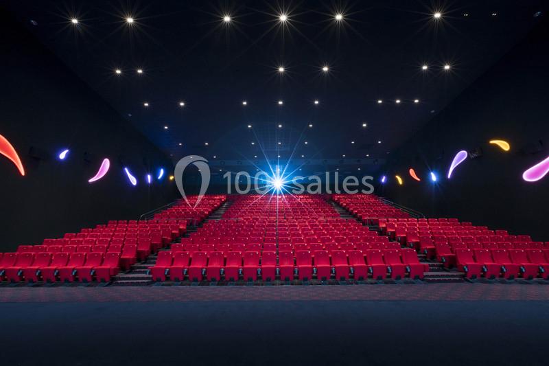 Salle de cinéma vide avec rangées de sièges rouges et éclairage tamisé, un projecteur allumé au fond.