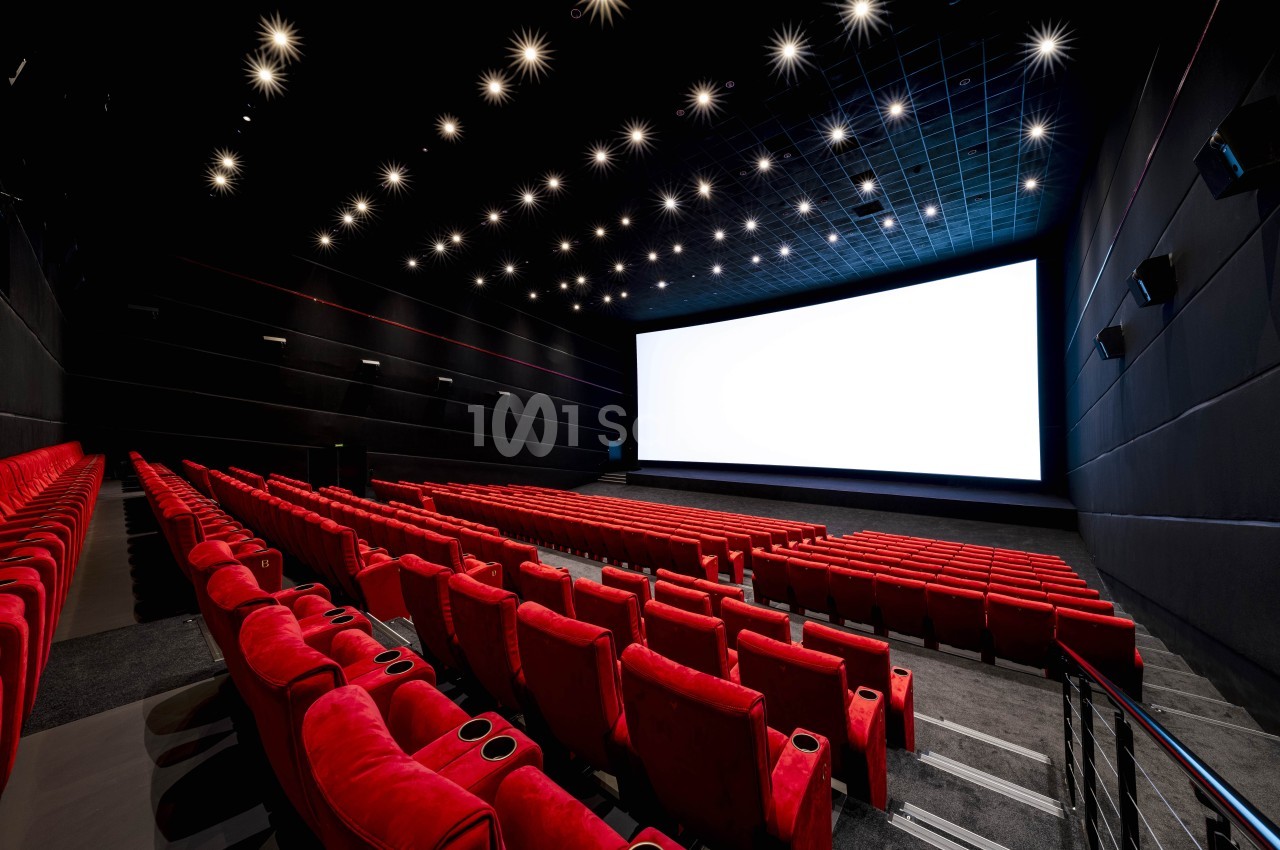 Salle de cinéma vide avec des rangées de fauteuils rouges et un grand écran blanc allumé.