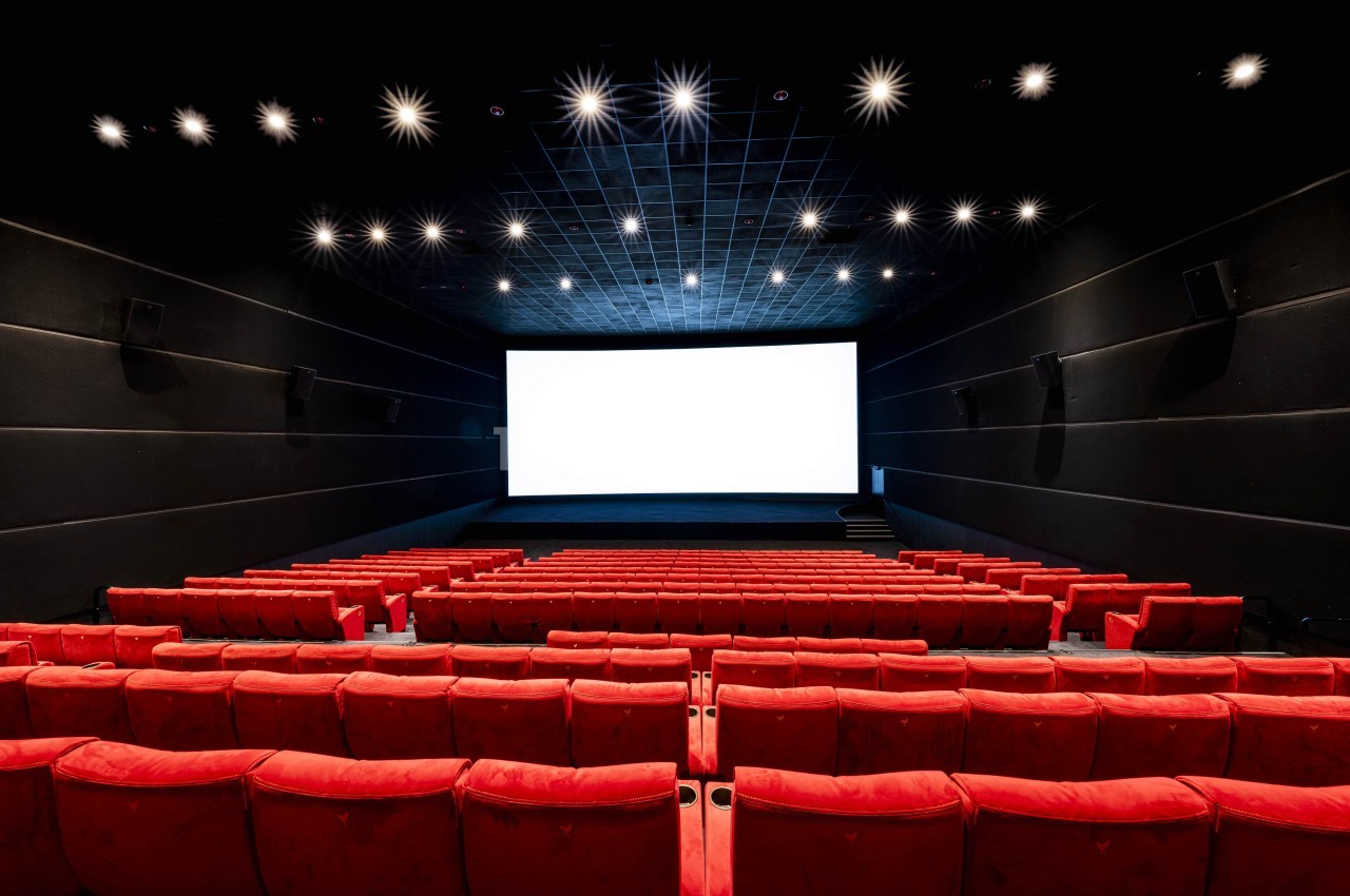 Salle de cinéma vide avec des rangées de fauteuils rouges et un grand écran blanc allumé.