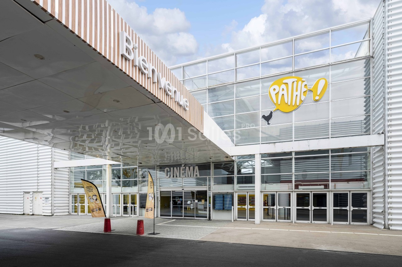 Entrée principale d'un cinéma Pathé avec une façade vitrée et des panneaux publicitaires devant.