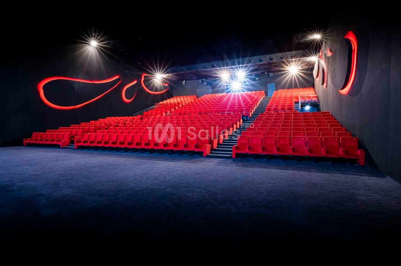 Salle de cinéma vide avec des rangées de sièges rouges et des éclairages muraux décoratifs rouges.