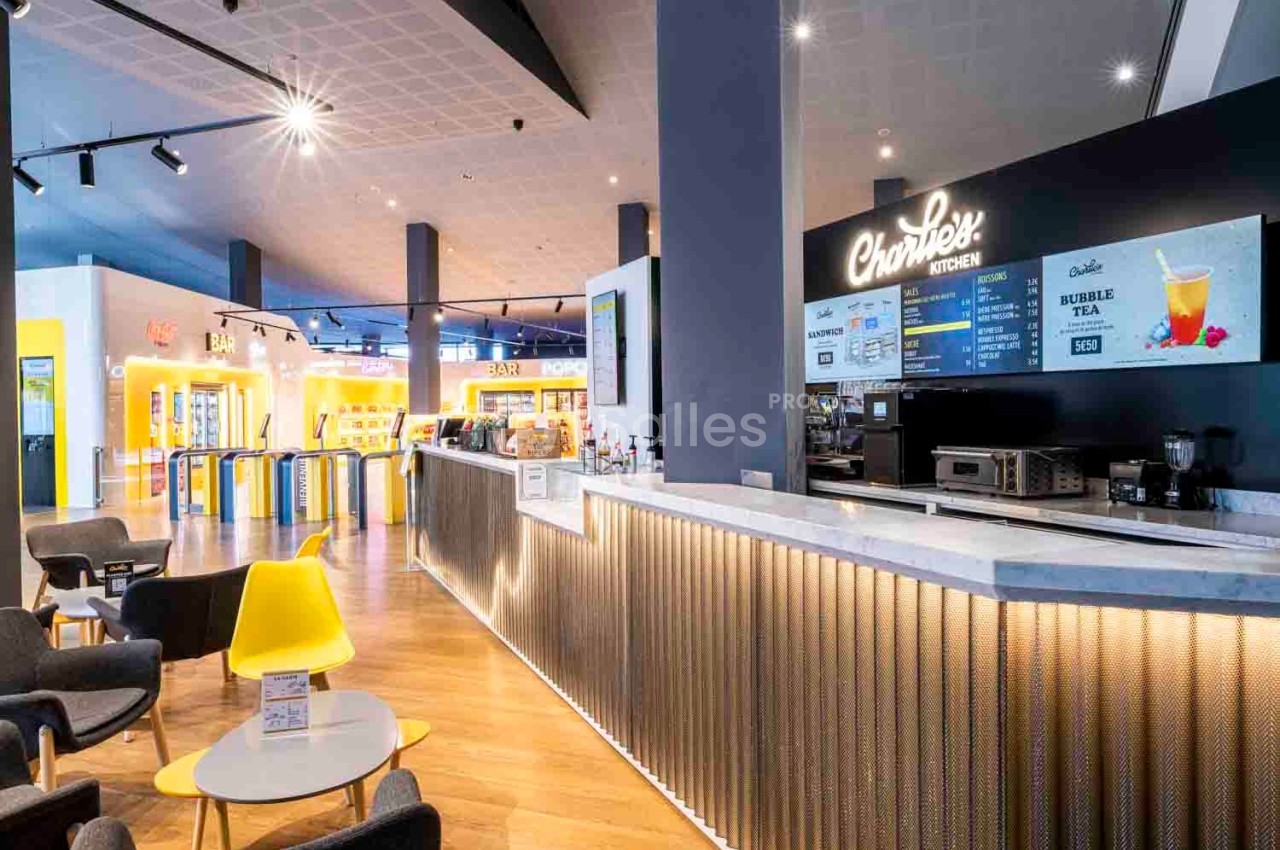 Comptoir de restauration moderne avec menu affiché, chaises colorées et éclairage lumineux dans un espace ouvert.