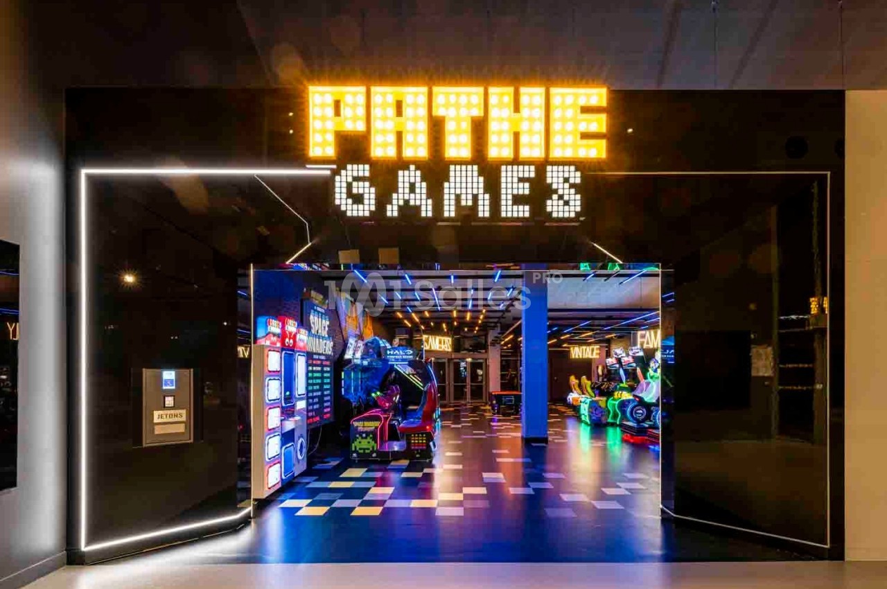 Entrée d'une salle d'arcade moderne avec enseigne lumineuse ’Pathé Games’ et jeux colorés à l'intérieur.