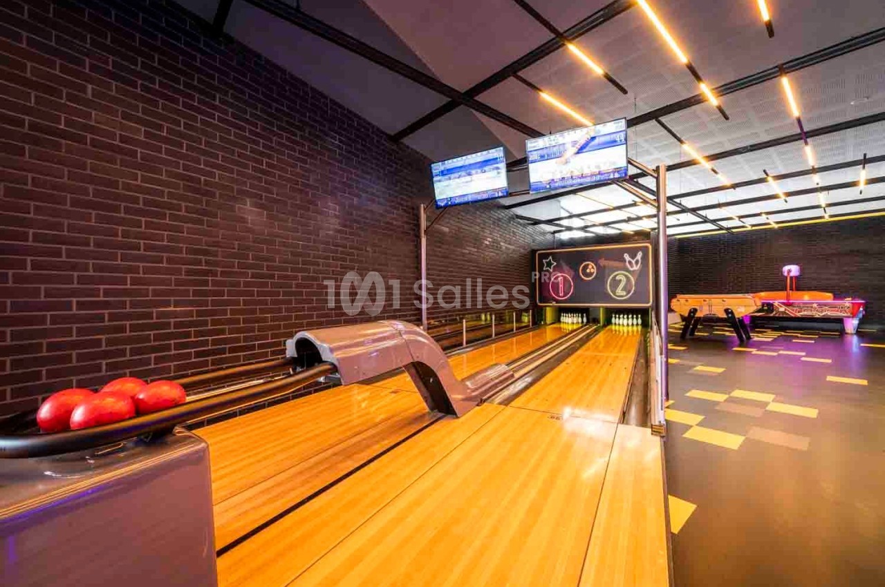 Piste de bowling avec boules rouges prêtes à l'emploi, écrans d'affichage et décor moderne en briques.