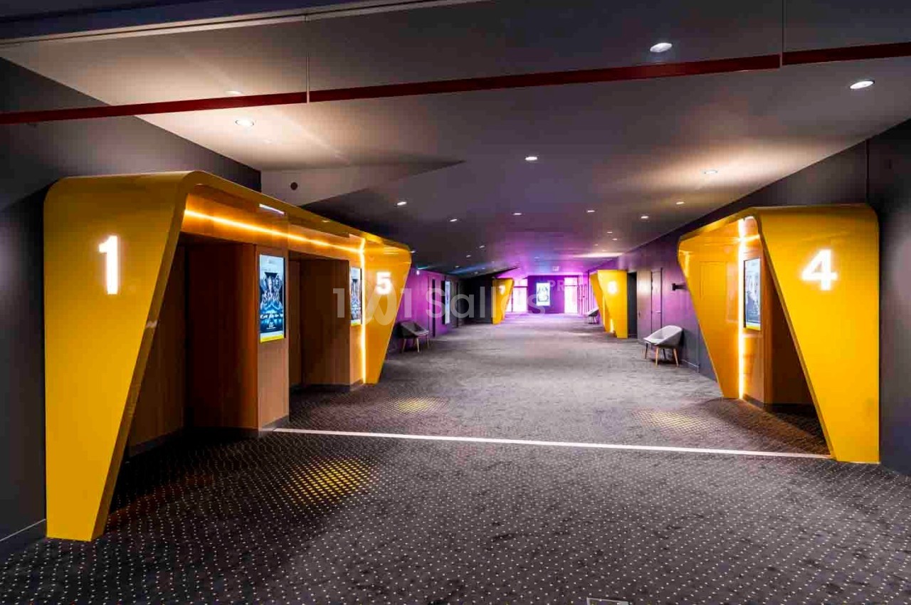 Couloir d'un cinéma avec des entrées de salles numérotées en jaune et éclairage tamisé.