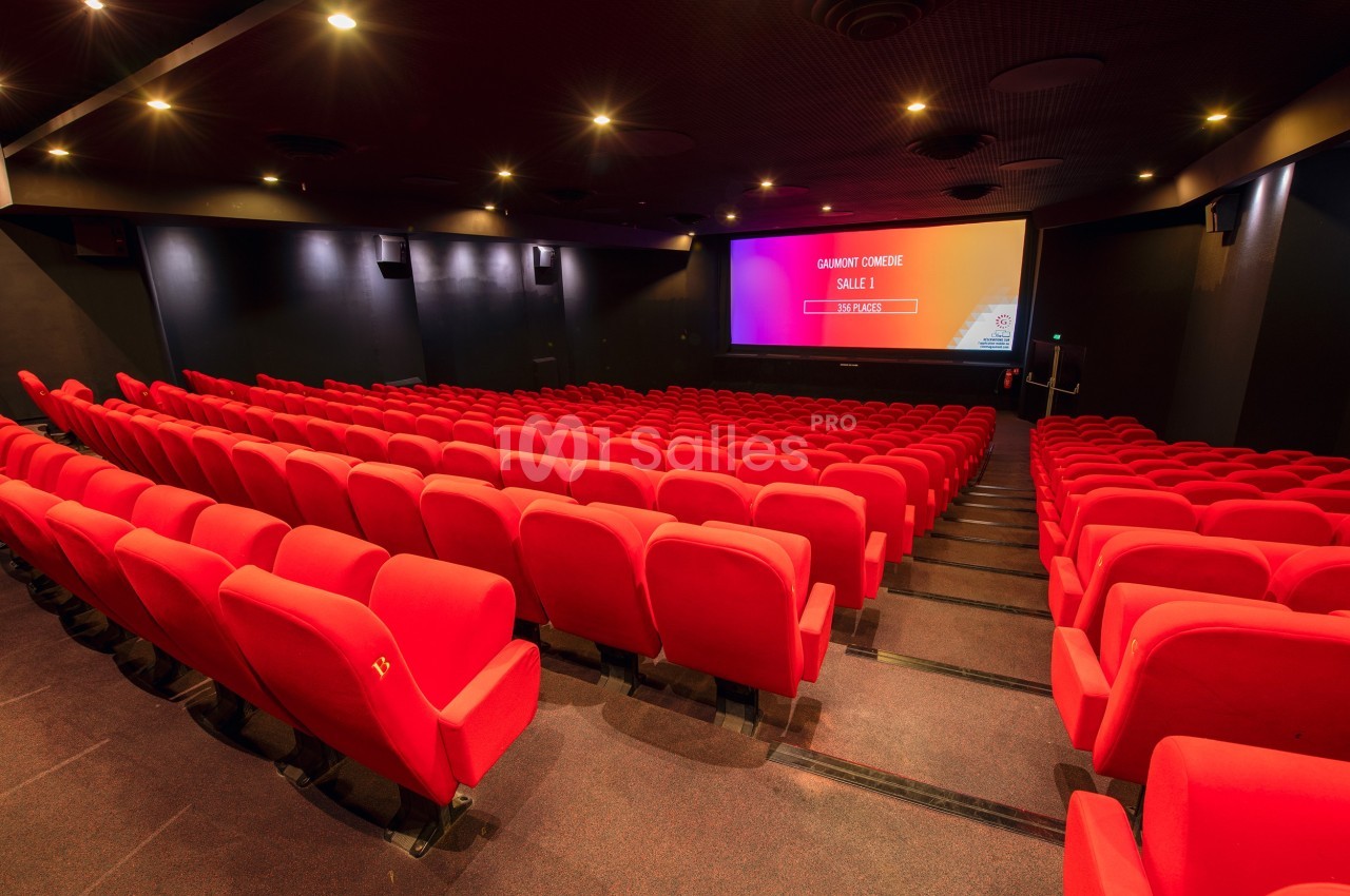 Salle de cinéma vide avec rangées de fauteuils rouges et un écran allumé affichant ’Grande Comédie - Salle 1’.