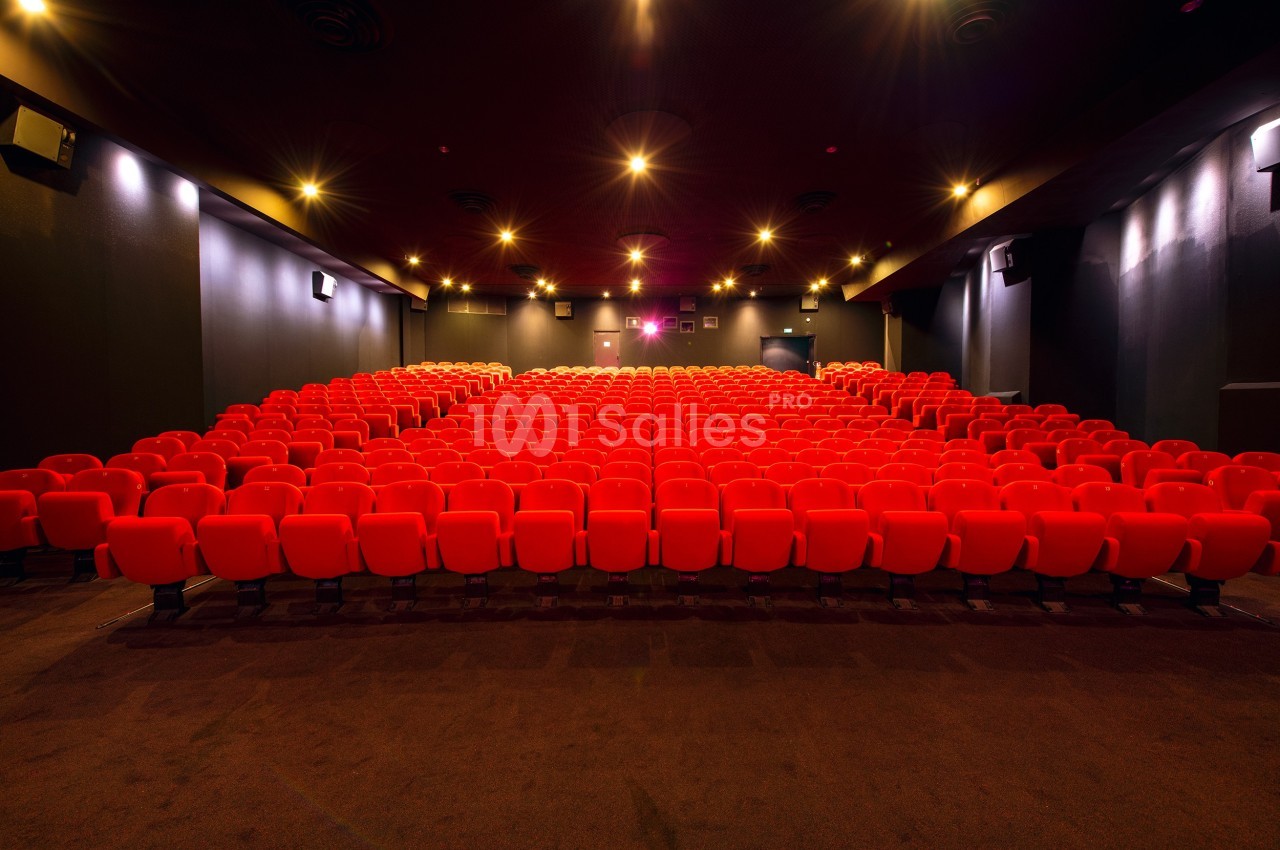 Salle de cinéma vide avec des rangées de fauteuils rouges alignés et un éclairage tamisé.